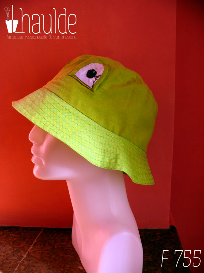 Bob grenouille avec des yeux en tissu cousus dessus. Le haut du bob est en tissu vert anis, le rebord dans un tissu un peu plus clair vert acide avec des lignes de losanges un peu plus foncées Vu de profil sur une tête de mannequin
