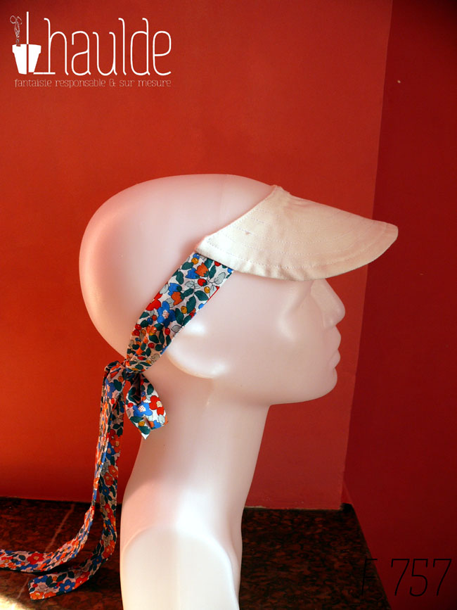 Visière en coton blanc surpiqué nouée à l'arrière de la tête avec des rubans blancs imprimés de fleurs multicolores à dominante rouge et bleu Vue de profil sur une tête de mannequin