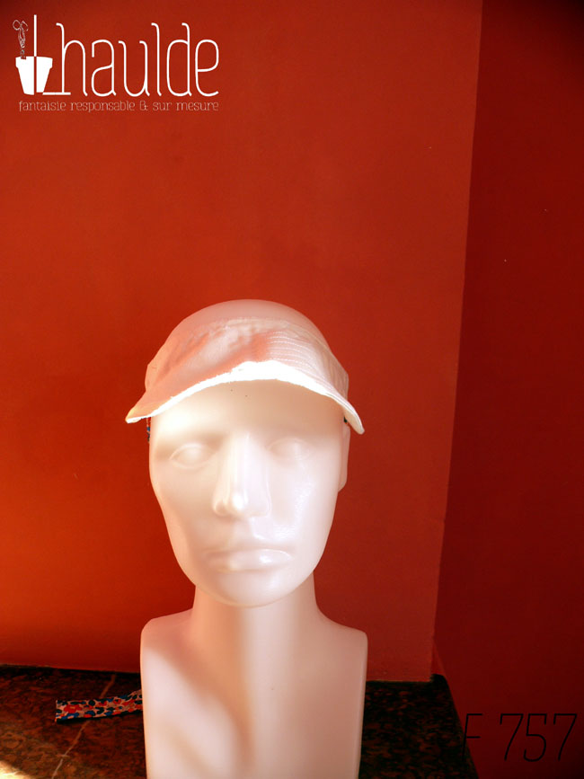 Visière en coton blanc surpiqué nouée à l'arrière de la tête avec des rubans blancs imprimés de fleurs multicolores à dominante rouge et bleu Vue de face sur une tête de mannequin