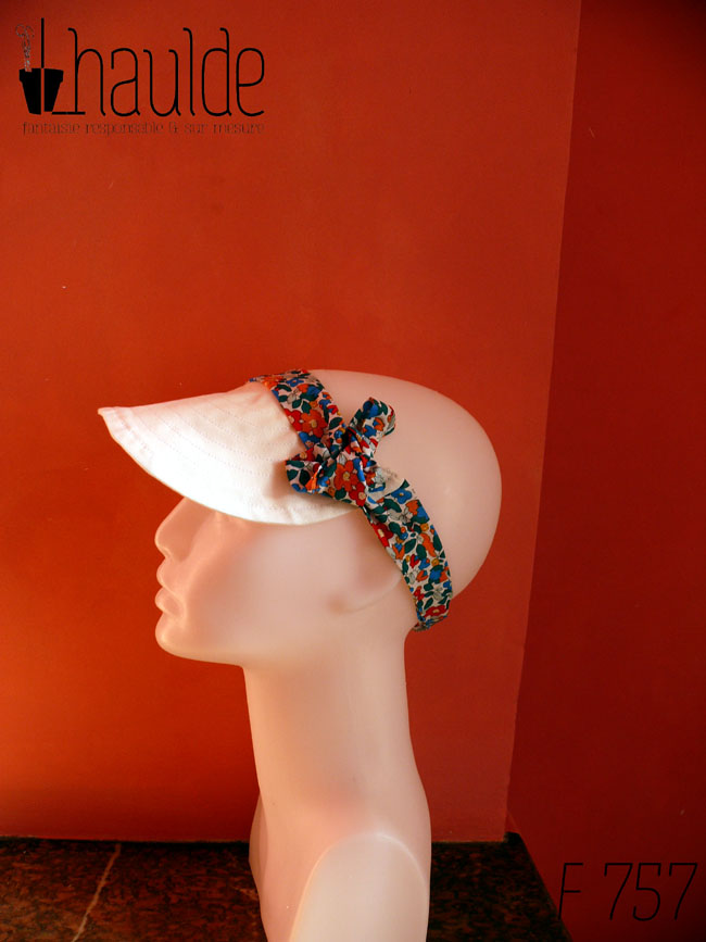 Visière en coton blanc surpiqué nouée sur le dessus de la tête avec des rubans blancs imprimés de fleurs multicolores à dominante rouge et bleu Vue de profil sur une tête de mannequin