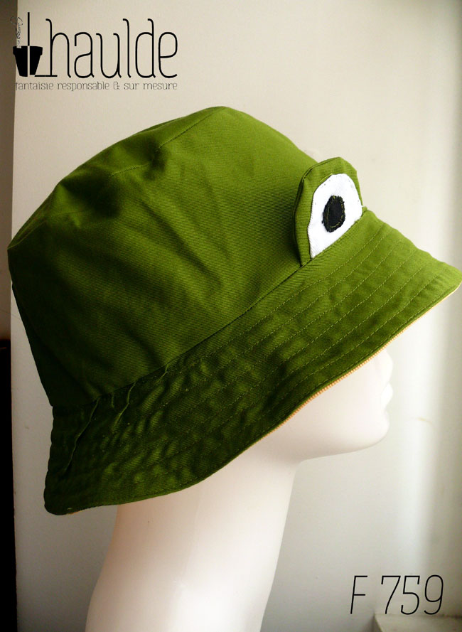 Bob grenouille vert avec des yeux en tissu cousus dessus L'intérieur est jaune Vu de profil sur une tête de mannequin