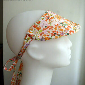 Visière à nouer en tissu blanc imprimé de fleurs oranges et roses, les brides sont également en tissu imprimé Vue de profil sur une tête de mannequin