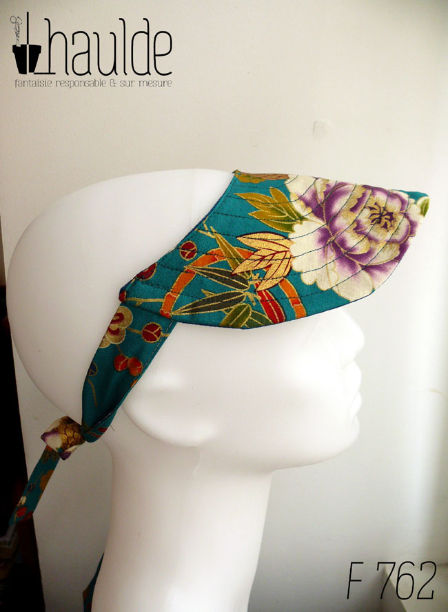Visière à nouer en tissu bleu paon imprimé fleuri d'esthétique chinoise, dahlias et autres fleurs multicolores rehaussées de doré Les brides sont en tissu imprimé Vue de profil sur une tête de mannequin