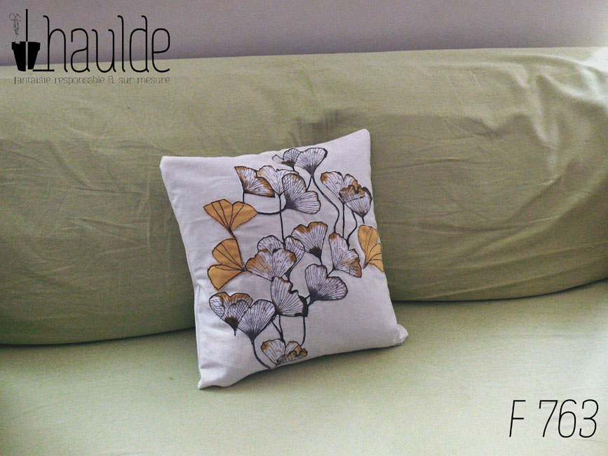 Housse de coussin blanc cassé avec des appliqués en tissu imprimé feuilles de ginkgo translucide et d'appliqués en forme de feuille de ginkgo en sergé jaune orangé surpiqué pour faire les nervures Vu posé sur un canapé vert pâle