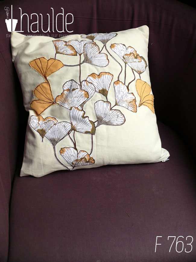 Housse de coussin blanc cassé avec des appliqués en tissu imprimé feuilles de ginkgo translucide et d'appliqués en forme de feuille de ginkgo en sergé jaune orangé surpiqué pour faire les nervures Vu sur un fauteuil violet