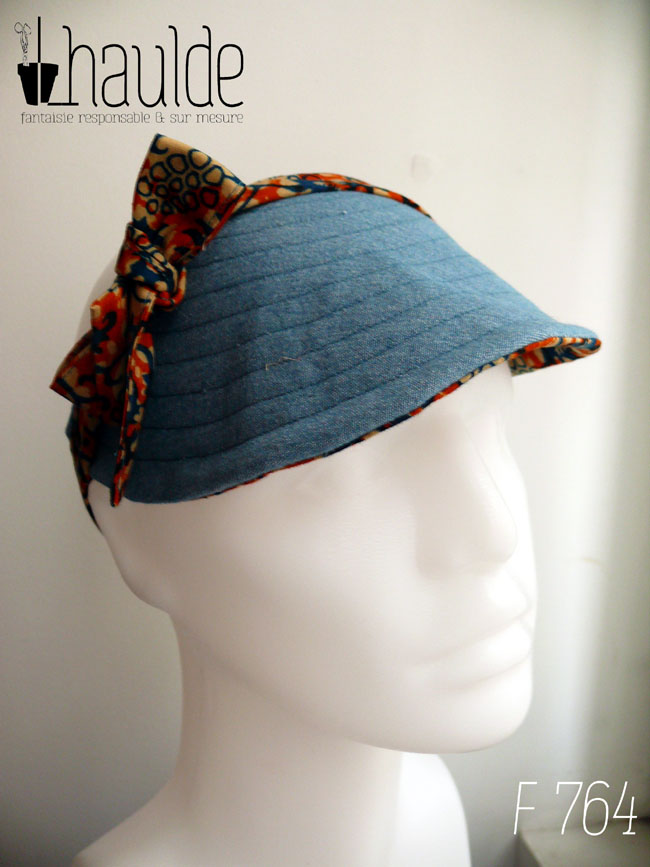 Vu sur l'envers, côté jean bleu uni Visière à nouer en coton orange imprimé de motifs végétaux stylisés bleu et écru Les brides sont en tissu imprimé Vue de face sur une tête de mannequin
