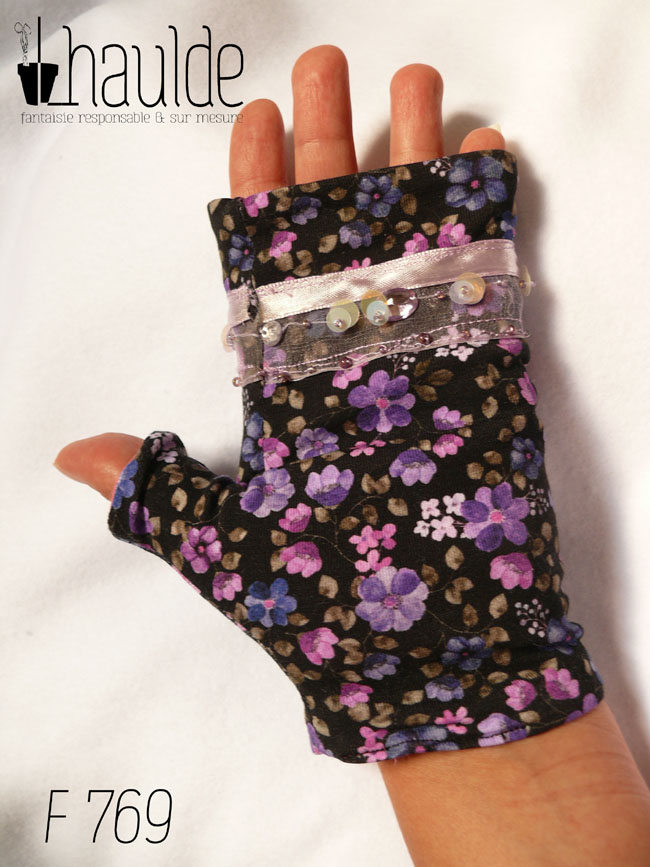 Mitaines en jersey noir imprimé de petites fleurs violettes, le pouce est couvert et au niveau des phalanges les mitaines sont garnies d'un galon d'organza transparent, garni d'un ruban rose pâle et de sequins ronds maintenus par des perles de rocailles Vue d'une mitaine portée, côté paume