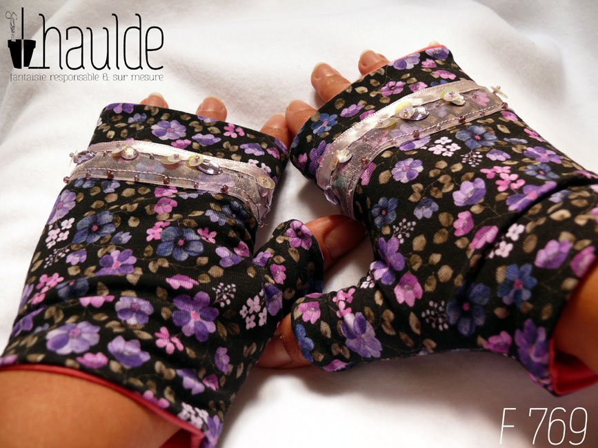 Mitaines en jersey noir imprimé de petites fleurs violettes, le pouce est couvert et au niveau des phalanges les mitaines sont garnies d'un galon d'organza transparent, garni d'un ruban rose pâle et de sequins ronds maintenus par des perles de rocailles Vue de la paire portée
