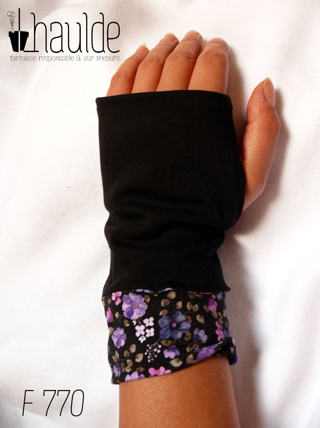 Mitaines en jersey noir, manchettes en tissu noir imprimé de petites fleurs violettes et en velours mauve Vue d'une mitaine portée, côté dos de la main avec la manchette déroulée au plus long, seul le jersey imprimé est visible