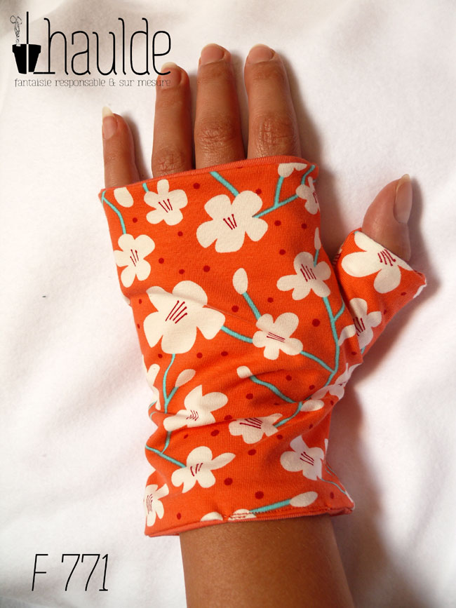 Mitaines en jersey corail imprimé de fleurs de cerisier blanches stylisées, avec des tiges turquoises Le pouce est couvert vue d'une mitaine portée, côté dos de la main