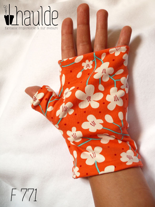 Mitaines en jersey corail imprimé de fleurs de cerisier blanches stylisées, avec des tiges turquoises Le pouce est couvert vue d'une mitaine portée, côté paume