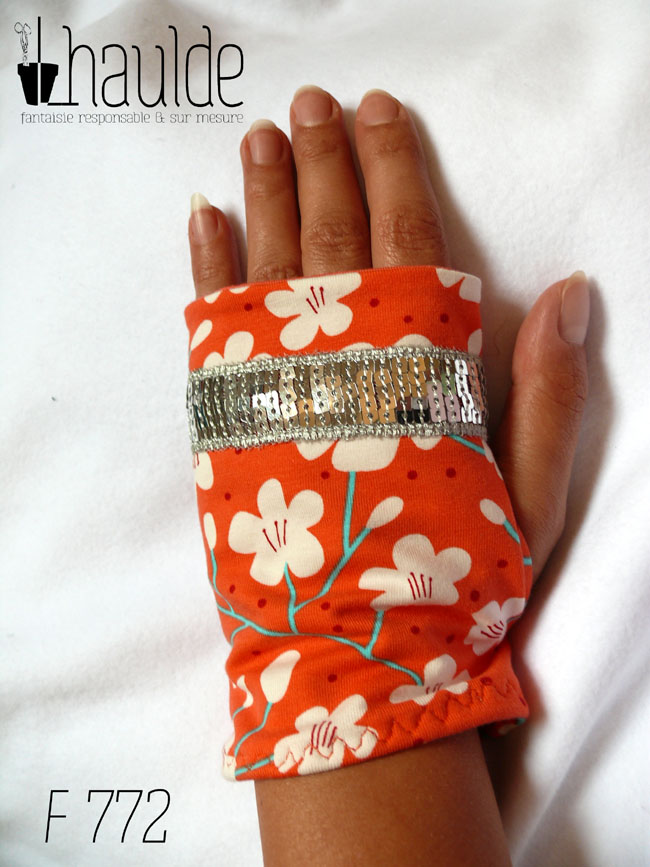 Mitaines en jersey corail imprimé de fleurs de cerisier blanches stylisées, avec des tiges turquoises Un galon de sequins argentés décore les mitaines au niveau des phalanges Vue d'une mitaine portée, côté dos de la main