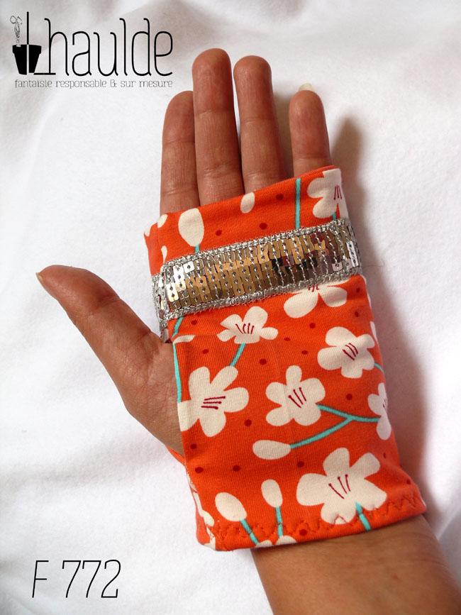 Mitaines en jersey corail imprimé de fleurs de cerisier blanches stylisées, avec des tiges turquoises Un galon de sequins argentés décore les mitaines au niveau des phalanges Vue d'une mitaine portée, côté paume