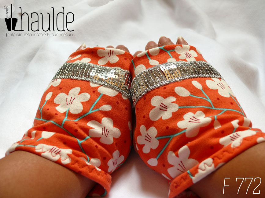 Mitaines en jersey corail imprimé de fleurs de cerisier blanches stylisées, avec des tiges turquoises Un galon de sequins argentés décore les mitaines au niveau des phalanges Vue de la paire portée