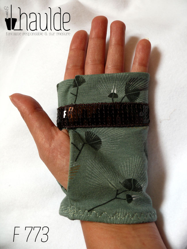 Mitaines en jersey vert céladon imprimé de motifs végétaux en forme de feuilles de palmes stylisées et aérées. Un galon de sequins carrés marrons garnit les mitaines à hauteur des phalanges Vue d'une mitaine portée, côté paume