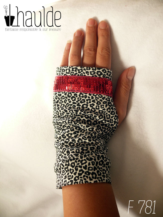 Paire de mitaines en jersey écru imprimé de petits motifs léopard noir. Avec au niveau des phalanges un galon de sequins carrés rouge fraises sur 5 rangs vue de dessus côté dos de la main, elles vont de la première phalange jusqu'à en-dessous du poignet