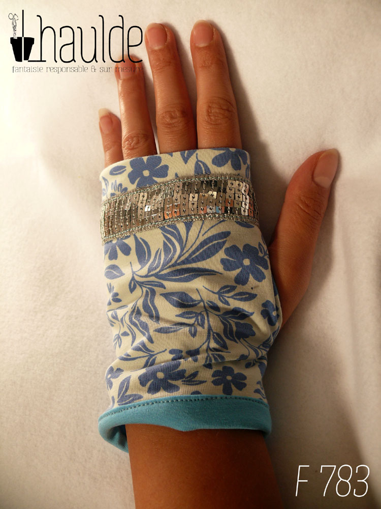 Paire de mitaines en jersey blanc imprimé de motifs floraux bleus en silhouette uni, décorée au niveau des phalanges d'un galon de sequins carrés argentés sur 5 rangs. Doublure en jersey bleu pastel qui ressort au niveau du poignet Vue d'une mitaine portée côté dos de la main