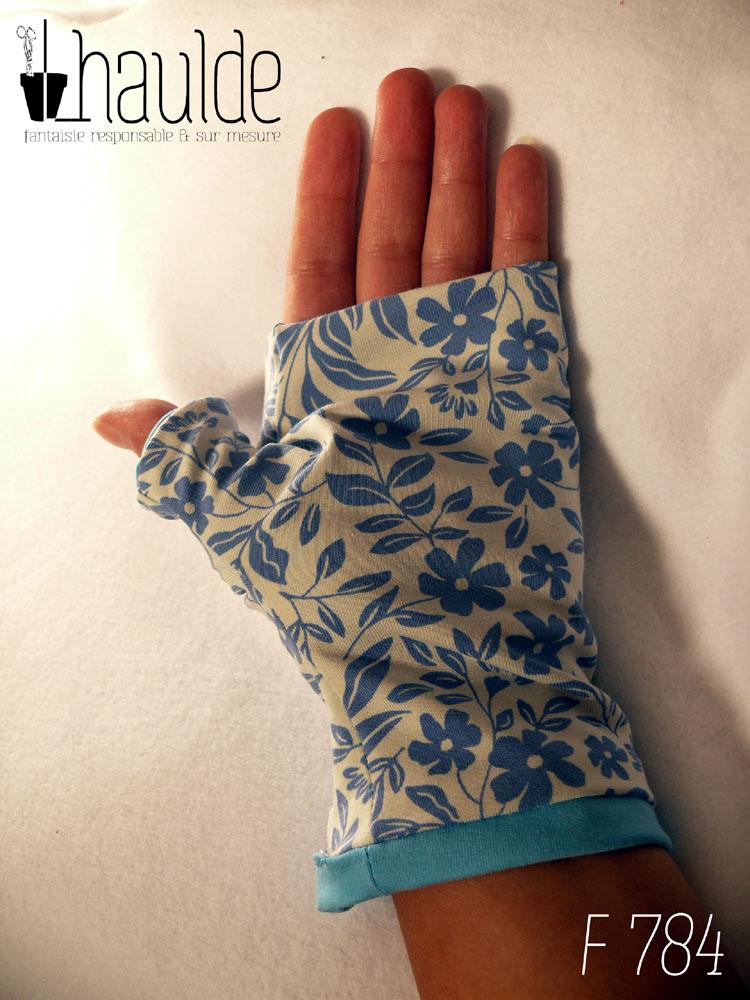 Paire de mitaines pouce long en jersey blanc imprimé de motifs floraux bleus en silhouette uni. Doublure en jersey bleu pastel qui ressort au niveau du poignet Vue d'une mitaine portée côté paume