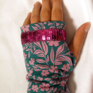 Paire de mitaines en jersey bleu pétrole imprimé de petites fleurs roses et décorée au niveau des phalanges d'un galon de sequins carrés fuchsia sur 5 rangs. vue de dessus côté dos de la main