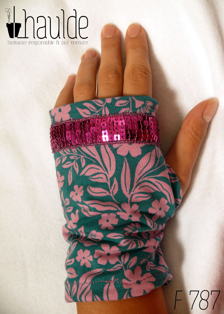 Paire de mitaines en jersey bleu pétrole imprimé de petites fleurs roses et décorée au niveau des phalanges d'un galon de sequins carrés fuchsia sur 5 rangs. vue de dessus côté dos de la main