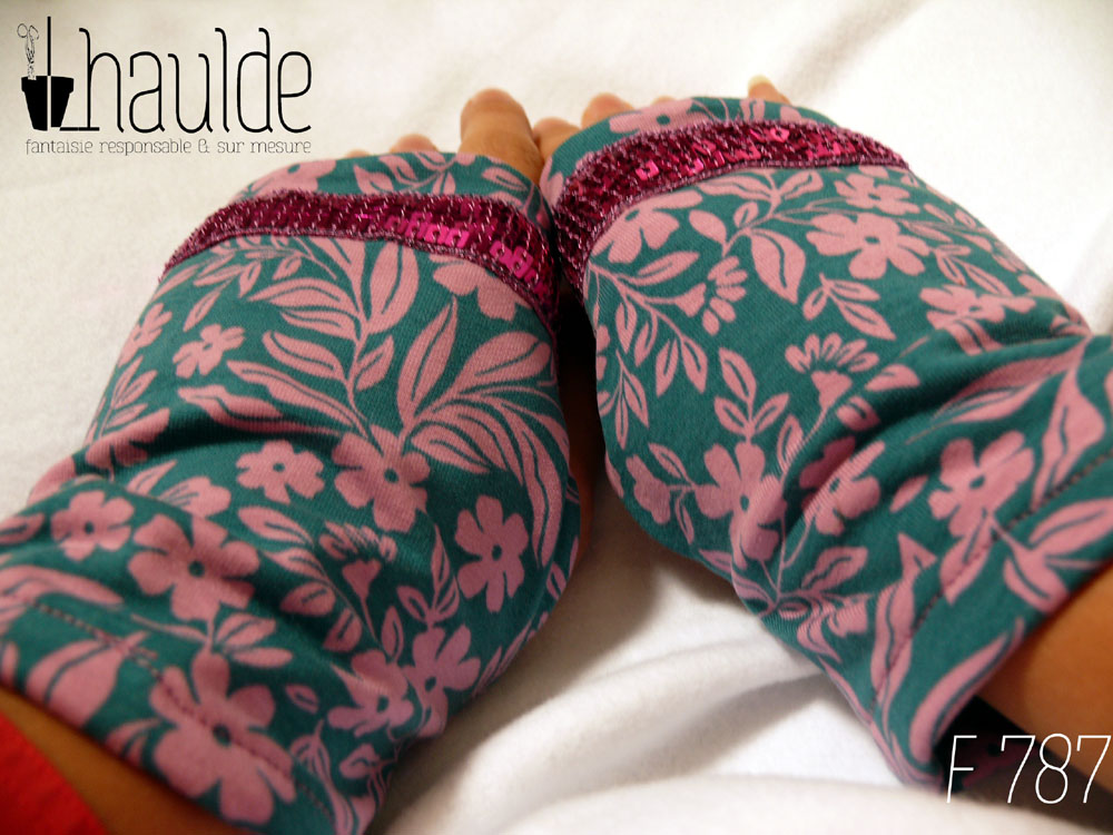 Paire de mitaines en jersey bleu pétrole imprimé de petites fleurs roses et décorée au niveau des phalanges d'un galon de sequins carrés fuchsia sur 5 rangs. vue de la paire portée