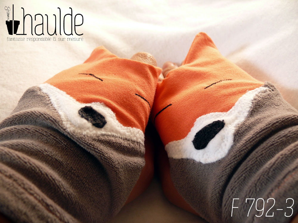 Paire de mitaines en forme de tête de renard. Côté doigts la tête avec les oreilles qui dépassent, en jersey orange, les yeux sont deux lignes noires brodées, le museau noir sur fond blanc est en polaire et le bas de la mitaines est en velours gris. Vue de la paire portée