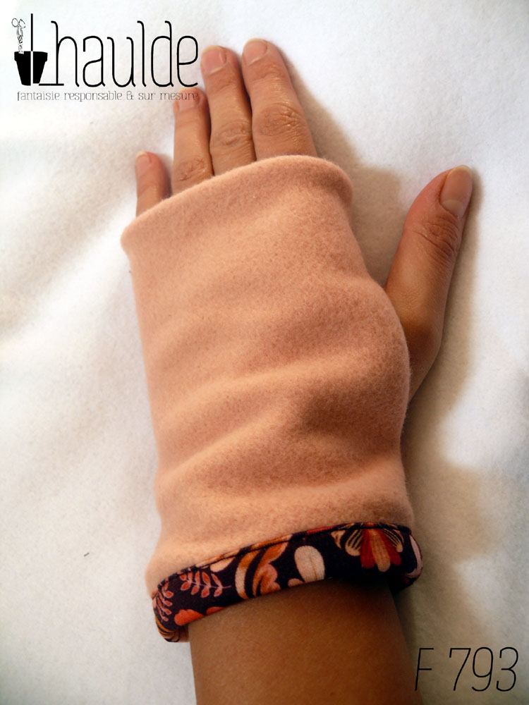Envers de la mitaine en polaire rose, une bande de jersey imprimé au niveau du poignet Paire de mitaines en jersey rouge bordeaux foncé imprimé de motifs végétaux et floraux agencés de façon symétrique dans les tons orangés Vue d'une mitaine portée, côté dos de la main