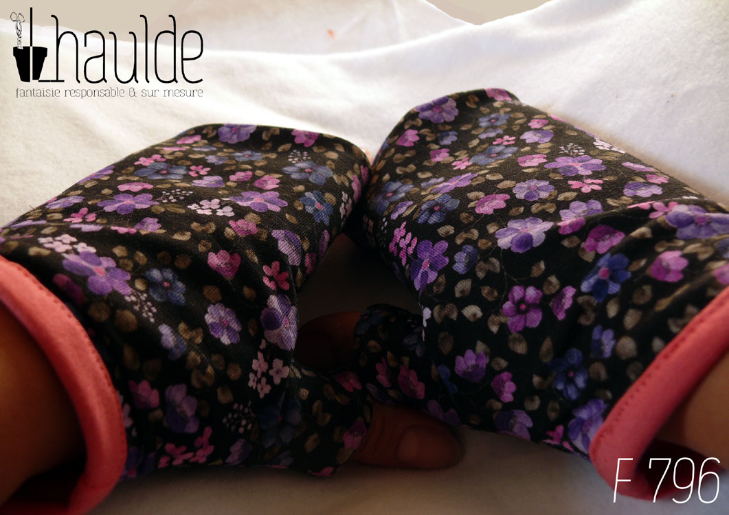 Mitaines avec pouce long en jersey noir imprimé petites fleurs violettes à pétales ronds, par 5 ou par 7 avec des mini fleurs rose très pâle ou rose à 4 pétales et de toutes petites feuilles kakis presque grises Le bord de la manchette est couvert de jersey rose Vue de la paire portée