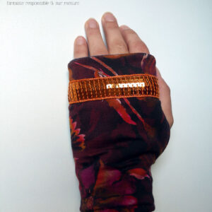Paire de mitaines en jersey marron imprimé de motifs floraux délavés comme dans une aquarelle très humide, dans des tons chauds allant de l'ocre au fuchsia, garnie d'un galon de sequins carrés oranges sur cinq rangs Vue d'une mitaine portée, côté dos de la main