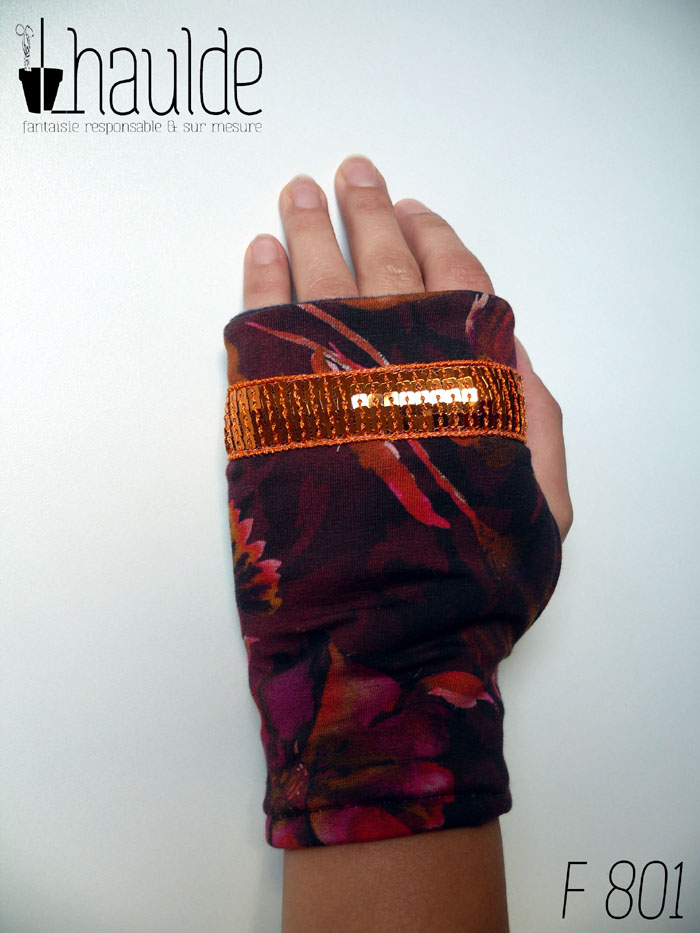 Paire de mitaines en jersey marron imprimé de motifs floraux délavés comme dans une aquarelle très humide, dans des tons chauds allant de l'ocre au fuchsia, garnie d'un galon de sequins carrés oranges sur cinq rangs Vue d'une mitaine portée, côté dos de la main