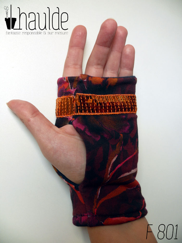 Paire de mitaines en jersey marron imprimé de motifs floraux délavés comme dans une aquarelle très humide, dans des tons chauds allant de l'ocre au fuchsia, garnie d'un galon de sequins carrés oranges sur cinq rangs Vue d'une mitaine portée, côté paume
